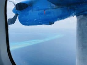 View from inside a seaplane in the Maldives. On the window we can see the airplane's propeller and the gorgeous blue water around a tiny island.