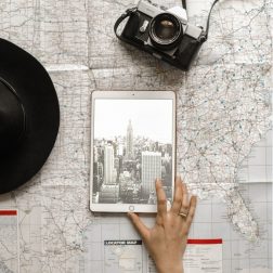 Flat Lay Photography of Person Touching Silver Ipad on World Map Chart Beside Black Hat